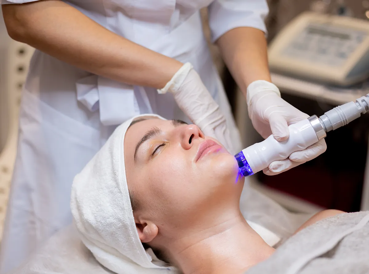 This image shows a person receiving a cosmetic facial treatment with a specialized device, possibly for rejuvenation or hair reduction 1200x890