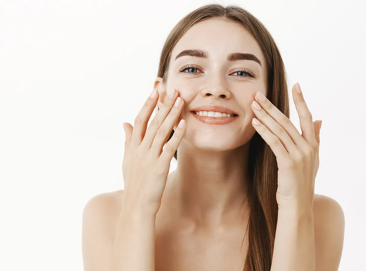 Smiling woman with clear skin touching her face after acne scar treatment 1200x890
